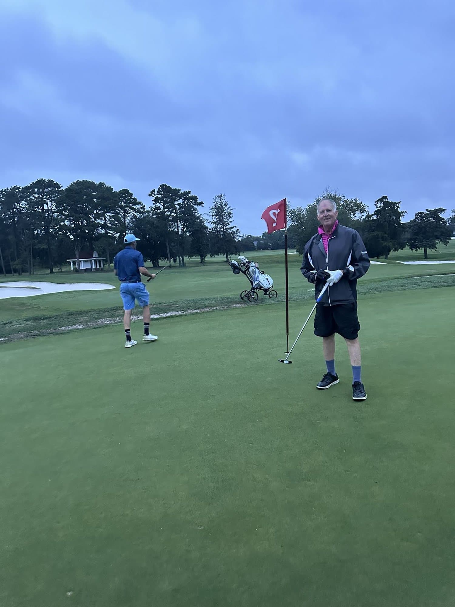 Golfers on a green at dusk, one holding the flagstick