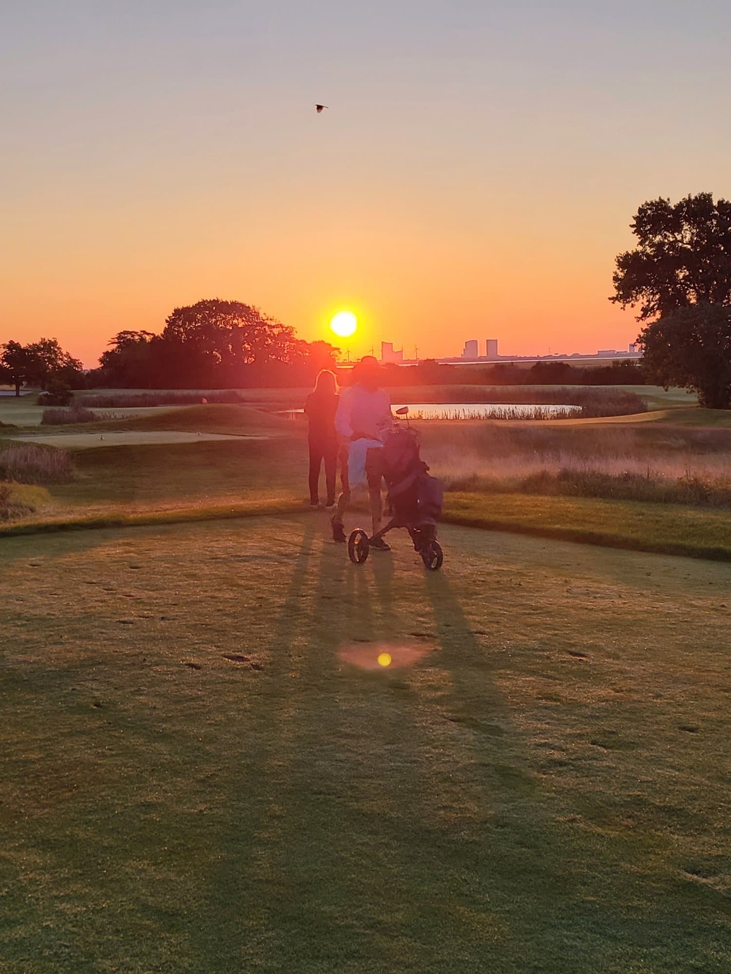 Two people walking a push cart toward a low sun, with the Atlantic City skyline on the horizon
