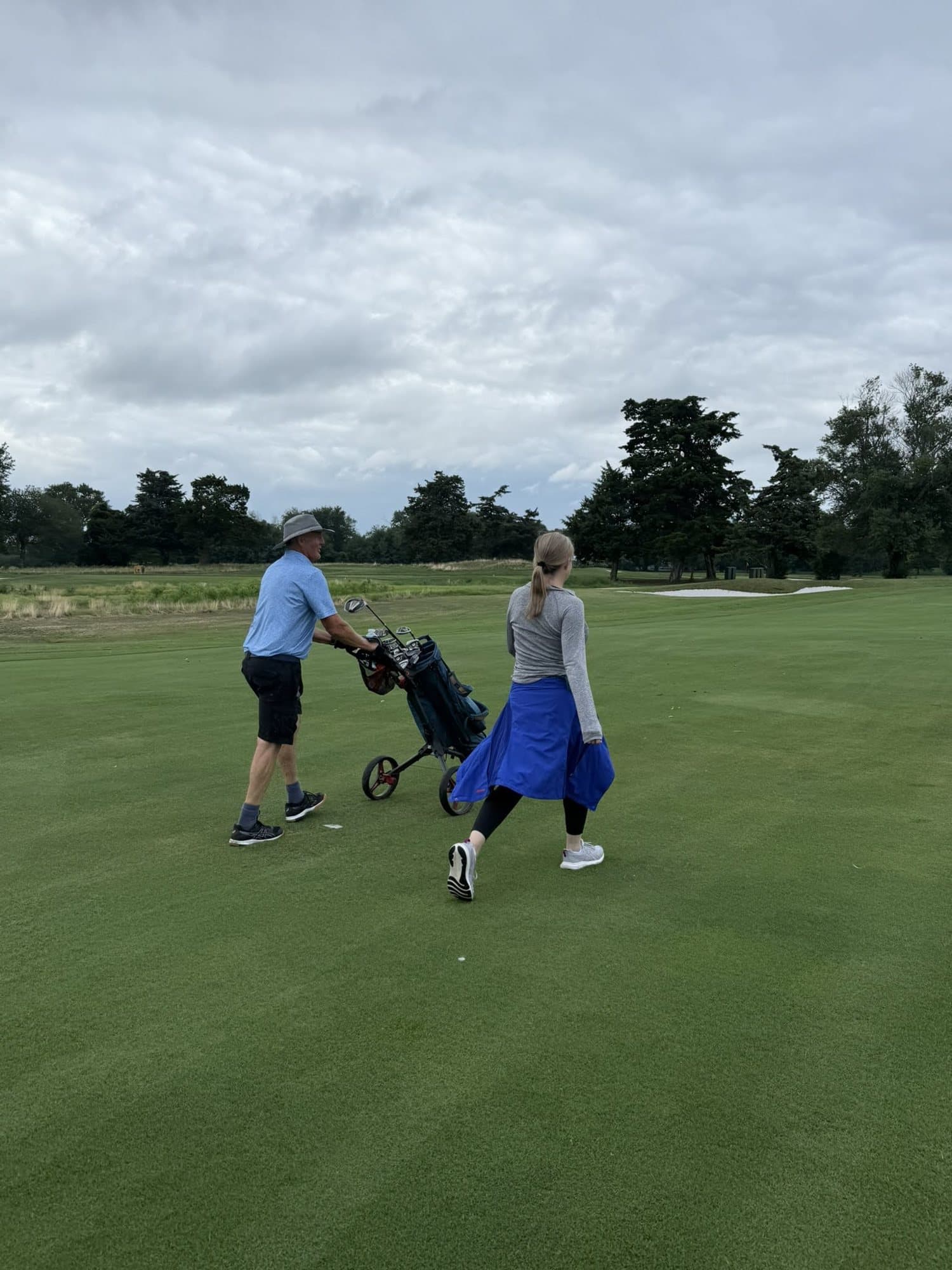 Two golfers pulling push carts down a fairway